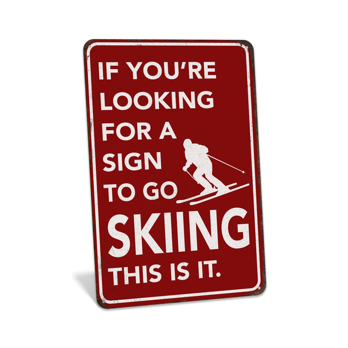 Rustic red metal skiing sign reading If You're Looking for a Sign to Go Skiing This Is It with skier silhouette